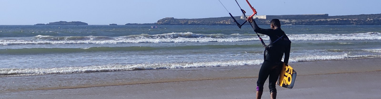 Coach de kitesurf sur la plage, allant à l'eau avec son aile et sa planche à Essaouira, Maroc.